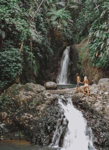 Tropical waterfall with lush vegetation and two people enjoying the serene scene