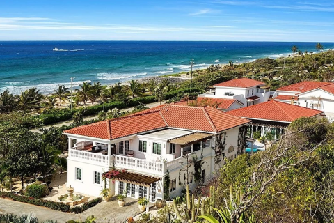 This image showcases a beautiful coastal scene with a luxurious residential property overlooking the ocean