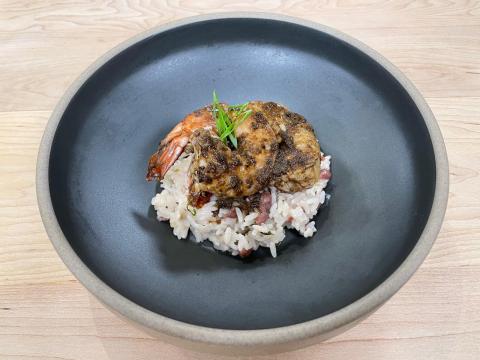 Cayman Tourism Board Contemporary Culinary Delight: Herb-Infused Rice with Seasoned Chicken and Prawn The image shows a gourmet dish consisting of rice topped with what appears to be a seasoned chicken thigh and a prawn