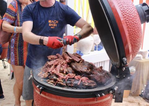 Cayman Tourism Board Summer Feast: Brisket Time at the Beachside BBQ This image captures a scene at a beachside cookout or barbecue event