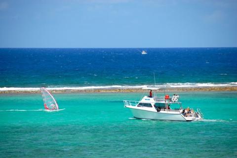 Cayman Tourism Board Leisure and Adventure in Tropical Paradise The image shows a vibrant coastal scene with clear blue waters and a partly sunny sky