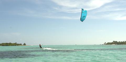 Cayman Tourism Board Thrills in Paradise: Kiteboarding Adventure in Tropical Waters The image shows a person kiteboarding in a tropical setting with clear, turquoise waters