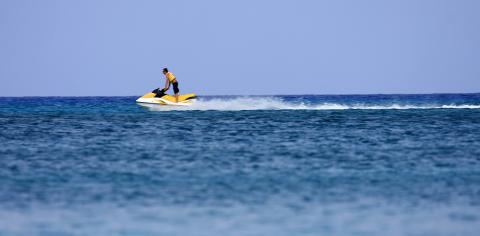 Cayman Tourism Board Thrills on the Horizon: Jet Ski Adventure on the Azure Sea This image shows a person riding a yellow jet ski on a large body of blue water