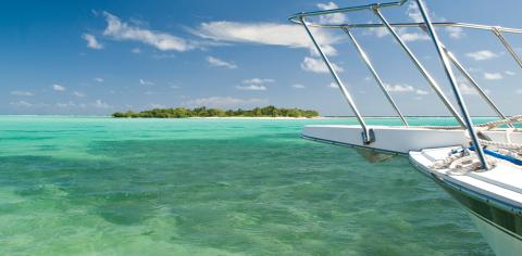 Cayman Tourism Board Serene Escape: Tropical Sailing Adventure This image features a view from a boat looking out towards a beautiful tropical landscape