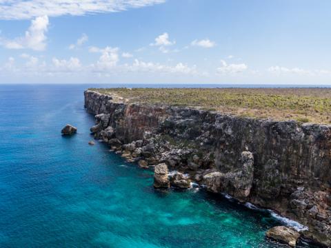 This image showcases a striking coastal landscape featuring a rugged, vertical cliff that drops steeply into a vividly turquoise sea