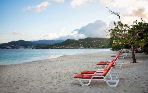 Sunset at beach with sun loungers, green foliage, calm sea, and hilly resort background