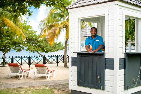 Man serving cocktail at beachside booth with lush backdrop and clear skies