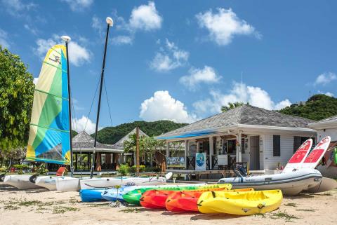 Colorful kayaks, paddleboards, and boats on a tropical beach with a dive shop.