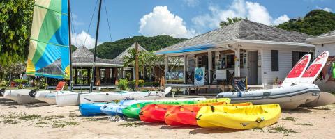 Tropical beach with sailboat, kayaks, and Eco Dive shop, perfect for water sports enthusiasts.