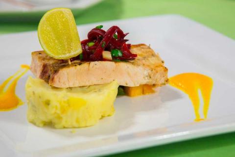 Gourmet grilled salmon with lime, vegetable garnish, and orange sauce on a white plate.