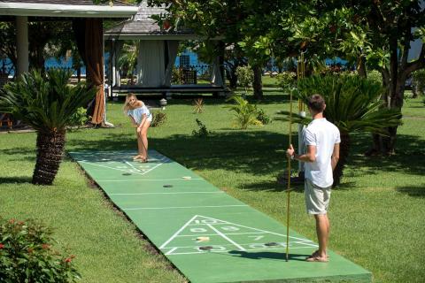 Two people playing shuffleboard in a tropical outdoor setting