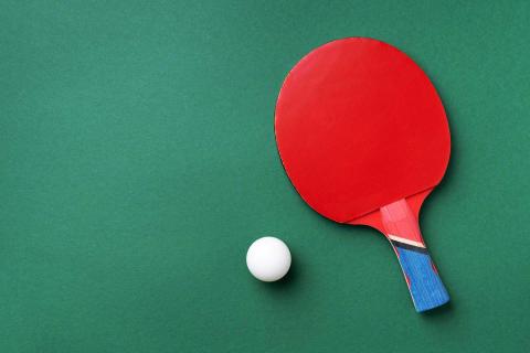 Red table tennis paddle and white ball on green background for sports theme.