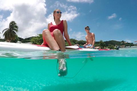 Couple relaxing on floating mat in clear turquoise sea with hills