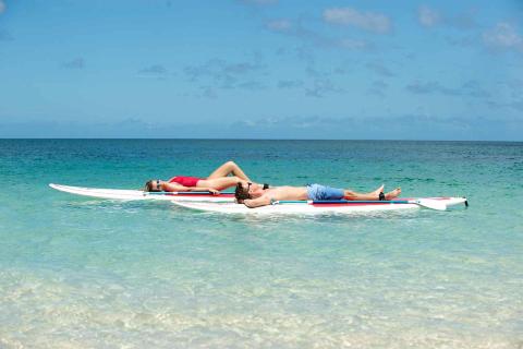 Man and woman sunbathing on paddleboards in clear blue ocean