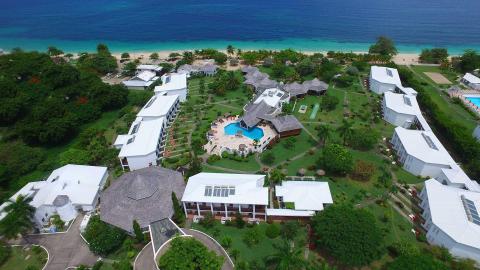 Aerial view of tropical beach resort with pool, sandy beach, and lush greenery