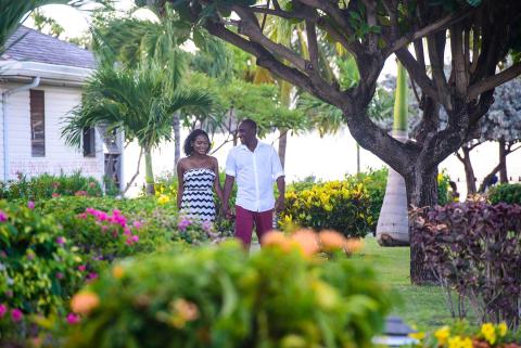 Couple walking in tropical garden, woman in chevron dress, man in white and red outfit.
