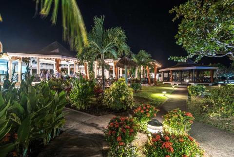 Tropical resort at night with colonial porch, lush gardens, and lit pathways.