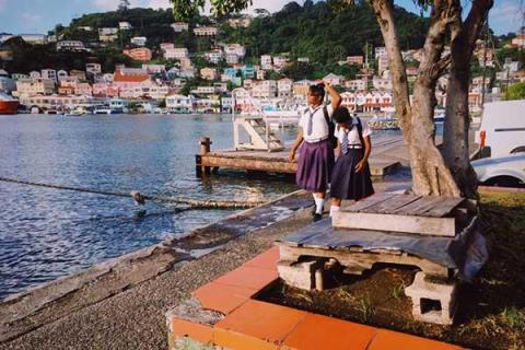Schoolchildren chatting by waterfront with scenic town and calm lake in background.