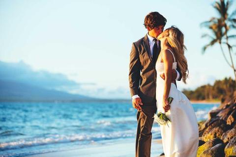Beach wedding kiss with couple in suit and gown at sunset.