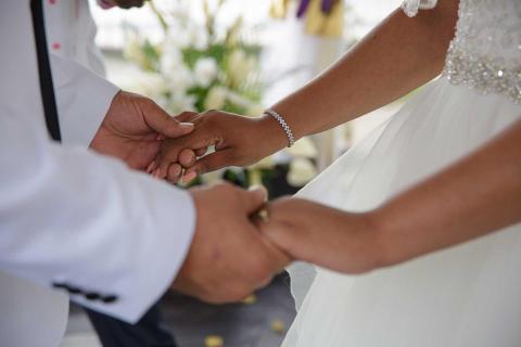Bride and groom holding hands at wedding with floral backdrop.