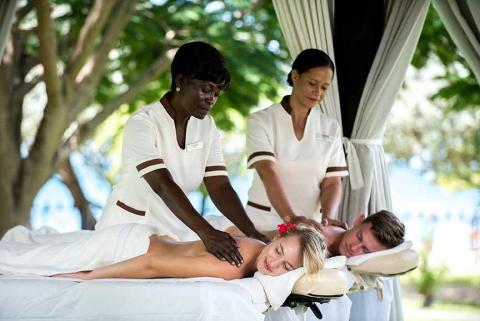 Couple enjoys outdoor massage at tropical resort with therapists in white