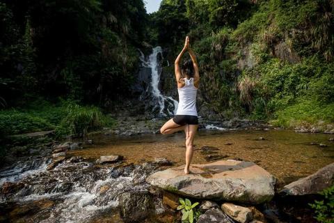 Person doing tree pose in yoga beside stream and waterfall in forest