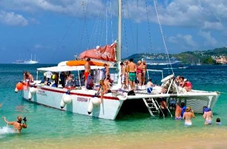 Group Enjoying Sunny Beach Day With Catamaran Group at beach with catamaran, clear sky, and swimmers, promoting active seaside recreation