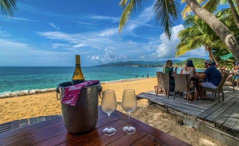 Tropical Beachfront With Wine And Ocean View Tropical beach scene with wine on table and people enjoying the sun.