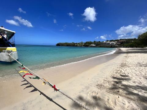 Serene Beach Scene With Docked Boat And Flags Serene beach scene with boat, colorful flags, and lush hillside under clear blue sky