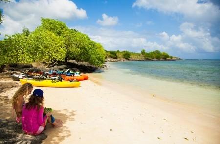Relaxing Beach Day With Kayaks And Sea View Two people on a sandy beach with colorful kayaks near trees, calm sea under partly cloudy sky.