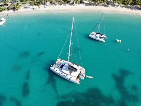 Tropical Beach With Boats And Clear Turquoise Water Aerial view of tropical beach with sailboats, yacht, and palm trees on clear turquoise waters