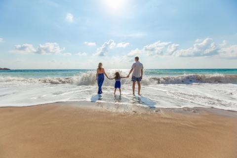 Family Enjoying Sunny Beach Day - Ocean View Family holding hands on beach facing ocean, wearing blue and white, sunny day with clear sky.