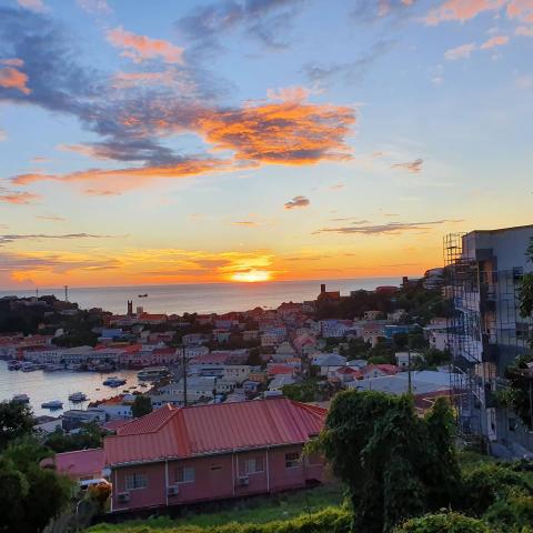 Sunset Over Coastal Town With Vibrant Sky And Boats Coastal town at sunset with vibrant sky, red-roofed buildings, and docked boats.