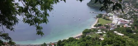 Scenic Aerial View Of Coastal Town And Bay Aerial view of a coastal town with boats in a turquoise bay surrounded by green hills.