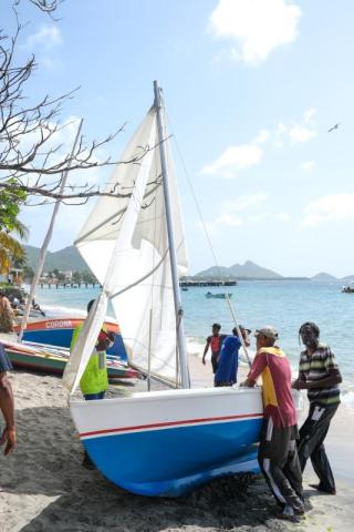 Group Launching Sailboat On Tropical Beach Group launching a sailboat on a sunny beach with distant mountains and pier.