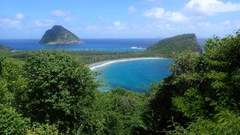 Stunning Tropical Island With Volcanic Hills Beach Tropical island beach with clear waters and volcanic hills, lush greenery in the foreground