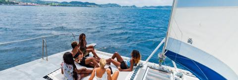Sailboat Adventure With Friends On Blue Ocean Group relaxing on sailboat with drinks, ocean view, and distant land.