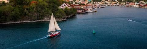 Scenic Harbor Town With Sailboats And Colorful Buildings Red sailboat and motorboat in a vibrant harbor with colorful town background.