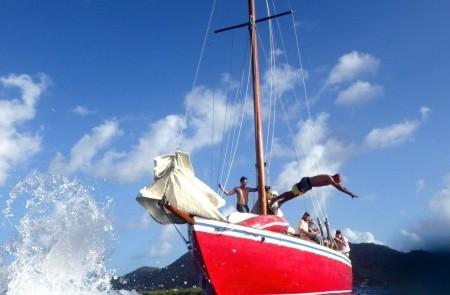 Red Sailboat Adventure In Tropical Waters Red sailboat with people and a diver in tropical seas under clear skies