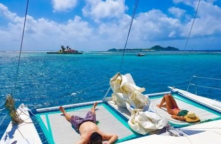 Relaxing Catamaran Day On Turquoise Sea Two people relaxing on a catamaran net in sunny tropical waters with islands in the background.