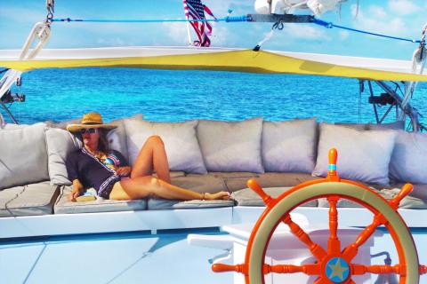 Luxury Catamaran Sailing With Ocean View Person relaxing on a catamaran with blue sky, turquoise waters, and American flag visible.