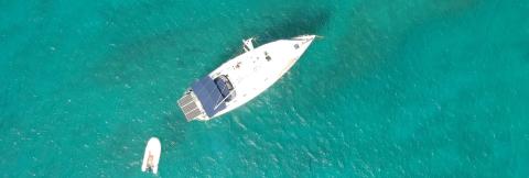 Solar-Powered Boat Tows Dinghy In Turquoise Waters Aerial view of white boat with solar panels towing dinghy over clear turquoise waters
