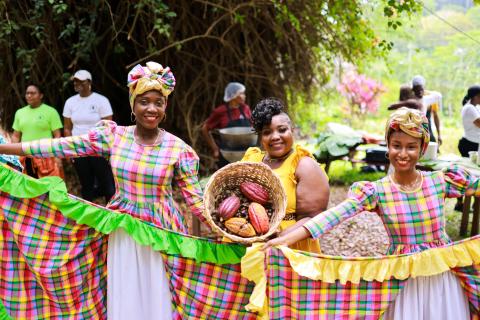 Women In Traditional Madras At Cocoa Festival Three women in madras attire with cocoa pods at a festival