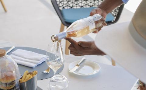 Person Pouring Wine At Outdoor Dining Table Person pouring white wine at outdoor dining table with appetizers.