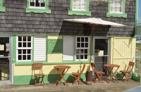Quaint Cafe With Outdoor Seating And Green Facade Quaint cafe with green facade, outdoor seating under umbrella, wooden tables for dining.