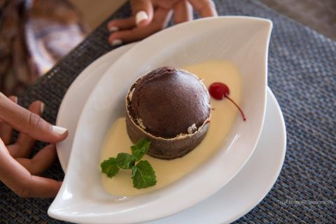 Chocolate Fondant With Vanilla Sauce In Elegant Setting Chocolate fondant with vanilla sauce, mint, and cherry on artistic plate in upscale setting.