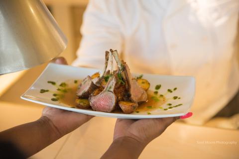 Elegant Lamb Chops Plating By Professional Chef Chef serves gourmet lamb chops with green sauce and roasted potatoes on elegant plate.