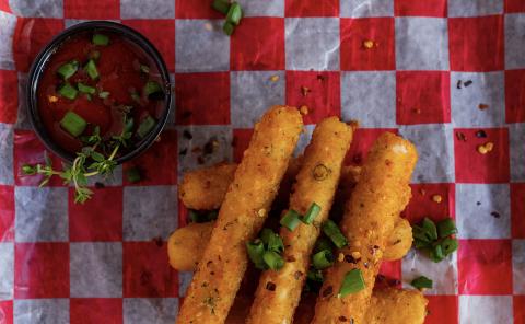 Spicy Mozzarella Sticks With Sauce On Checkered Paper Mozzarella sticks with spicy chili flakes and green onions, served with sauce.