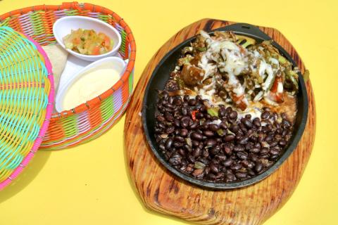 Delicious Fajitas With Sides On Themed Plate Colorful plate of fajitas with cheese, black beans, sour cream, and salsa on a wooden board.