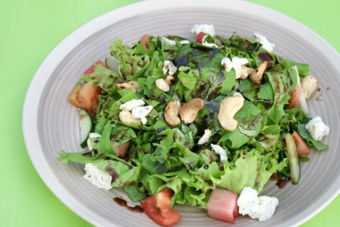 Fresh Mixed Green Salad With Feta And Nuts Fresh mixed salad with spinach, lettuce, tomatoes, cucumbers, feta, and cashews in a bowl.